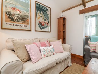 A sitting area with a beige sofa with cushions a wooden shelf a window with curtains and framed posters on the wall at Hay Loft Bolenowe Nr Portreath