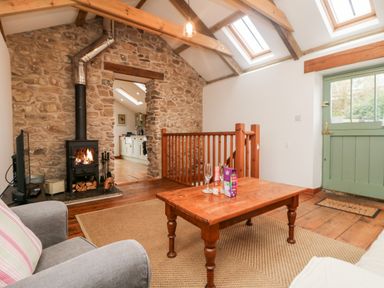 A seating area with a wooden coffee table and chairs near a wood burning stove and stone wall at Hay Loft Bolenowe Nr Portreath
