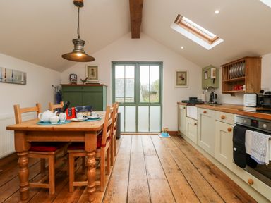 A kitchen dining area with wooden table and chairs next to a cabinet and kitchen counter at Hay Loft Bolenowe Nr Portreath