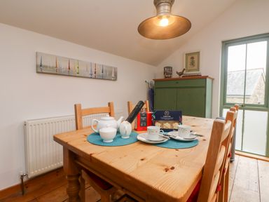 A dining room with a wooden table, four chairs, tea set, boxed food items, a green cabinet, and a window at Hay Loft Bolenowe Nr Portreath