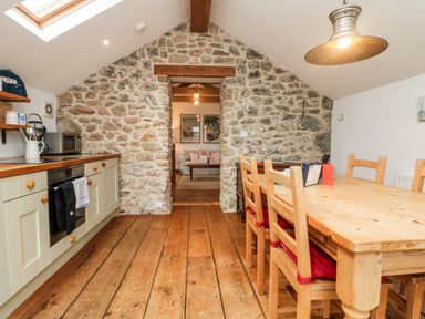 A kitchen with wooden floor and dining table next to a stone wall at Hay Loft in Bolenowe Nr Portreath