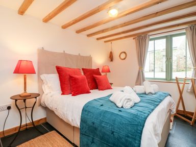 A bedroom with a double bed red pillows blue throw two bedside lamps and a window with curtains at Hay Loft Bolenowe Nr Portreath