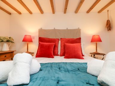 A bedroom with a bed with red pillows and blue blanket with rolled white towels on bed at Hay Loft Bolenowe Nr Portreath