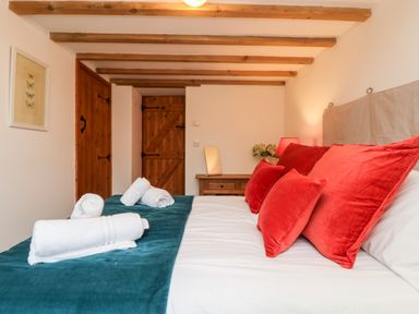 A bedroom with a bed with red pillows and white towels on a blue runner at Hay Loft in Bolenowe Nr Portreath