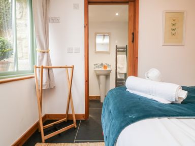 A bedroom with a bed and rolled towels next to a door leading to a bathroom with a sink and a towel rack at Hay Loft Bolenowe Nr Portreath
