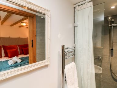 A bathroom with shower and towel rail and a reflection of a bedroom with pillows and towels at Hay Loft Bolenowe Nr Portreath