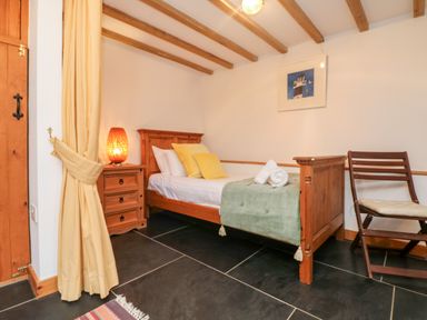 A bedroom with a wooden bed with pillows and a blanket a bedside table with a lamp a wooden chair and a framed picture on the wall at Hay Loft Bolenowe Nr Portreath