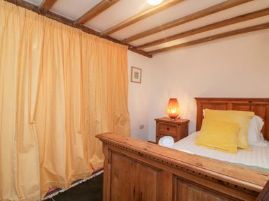 A bedroom with a wooden bed frame yellow pillows beside a wooden nightstand with a lamp and yellow curtains at Hay Loft Bolenowe Nr Portreath
