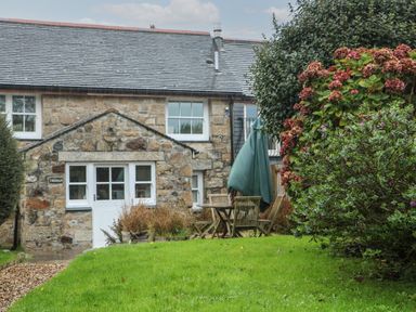 A stone cottage with a green lawn and outdoor wooden table and chairs at Trehan in St Ives