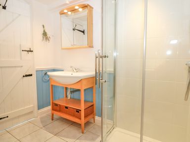 A bathroom with a wooden framed sink with a wicker basket underneath and a glass shower enclosure at Trehan in St Ives