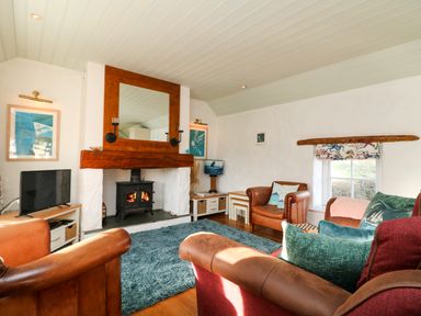 A living room with a wood burning stove under a large wooden framed mirror and leather armchairs at Trehan in St Ives