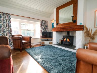 A living room with leather armchairs a wood burning stove a large mirror and a blue rug at Trehan in St Ives