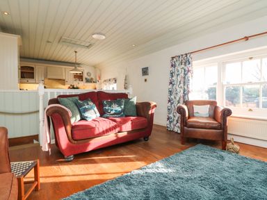 A living room with a red sofa and brown armchair near a window with patterned curtains at Trehan in St Ives