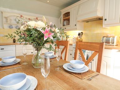 A dining table set with plates bowls and glasses with a vase of flowers in a kitchen at Trehan in St Ives