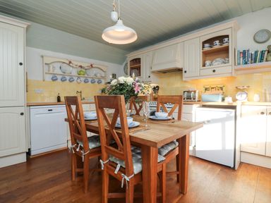 A kitchen with a wooden dining table and four chairs set with dishes and flowers at Trehan in St Ives