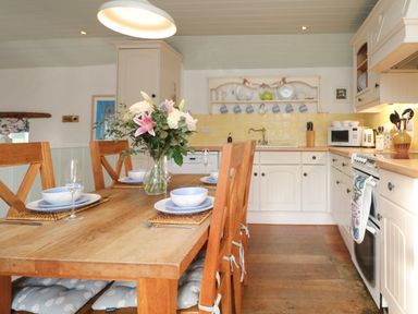A kitchen with a wooden dining table set with plates and glasses and a vase of flowers at Trehan St Ives