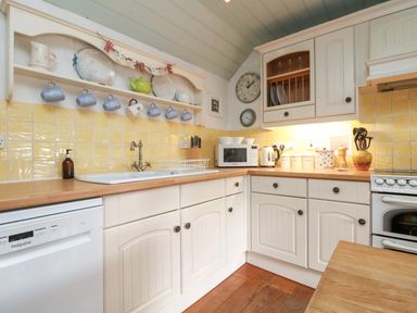 A kitchen with white cabinets yellow tiled backsplash dishwasher microwave kettle and stove at Trehan in St Ives