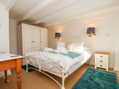A bedroom with a metal bed frame white wardrobe bedside table and blue rugs at Trehan in St Ives