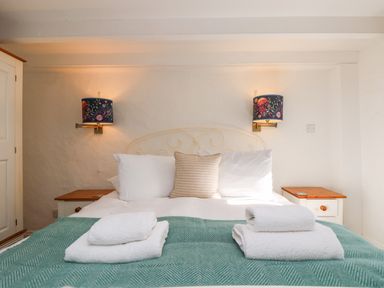A bedroom with a bed with pillows and folded towels on a green blanket and wall lights above each bedside table at Trehan in St Ives
