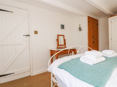 A bedroom with a white metal bed frame a blue blanket and folded towels on the bed a wooden dressing table with a mirror a white door and wooden closet doors at Trehan in St Ives
