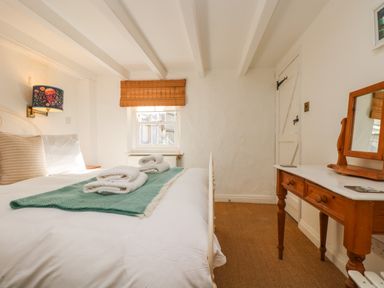 A bedroom with a bed, a window with a bamboo blind, and a wooden dressing table with a mirror at Trehan in St Ives