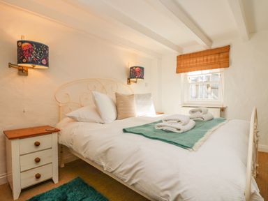 A bedroom with a double bed bedside tables towels on the bed and a window with a wooden blind at Trehan in St Ives