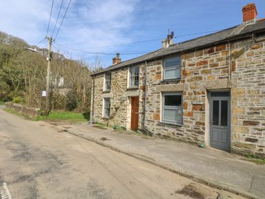 A stone cottage with two doors and windows on a quiet road near trees at Trevean in Portreath