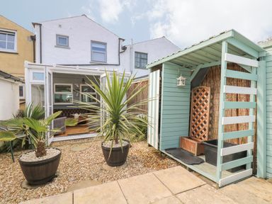 A backyard with potted plants gravel and a small wooden shed next to a white house with open glass doors at Trevean in Portreath