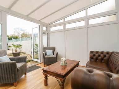 A conservatory with two armchairs a leather sofa and a wooden coffee table at Trevean in Portreath