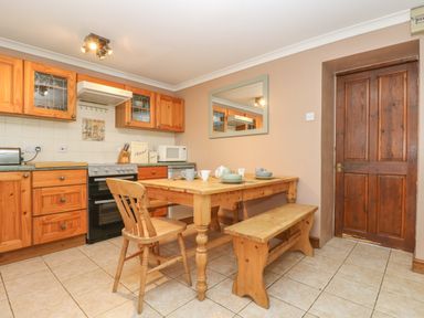 A kitchen with wooden cabinets a stove a wooden table with cups and a bench and chair at Trevean in Portreath