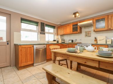 A kitchen with wooden cabinets a wooden dining table with dishes and cups and a dishwasher at Trevean in Portreath