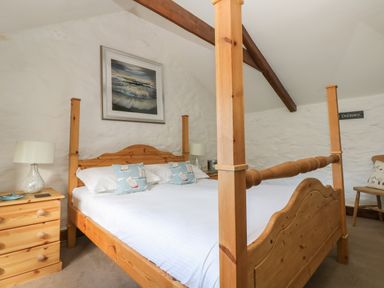 A bedroom with a wooden four-poster bed, bedside tables with lamps, and a framed seascape above the bed at Trevean in Portreath