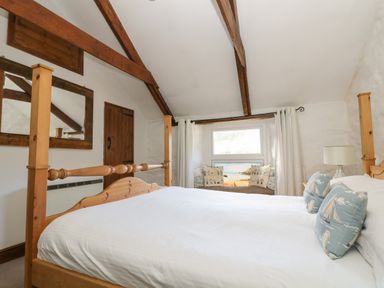 A bedroom with a wooden bed frame a window seat with cushions and exposed ceiling beams at Trevean in Portreath