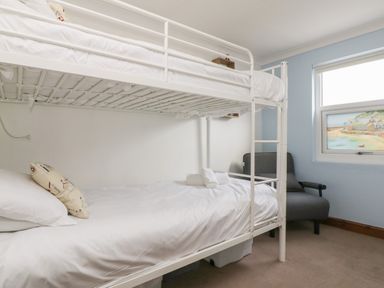 A bedroom with a white bunk bed a gray chair and a window with a coastal painting at Trevean in Portreath
