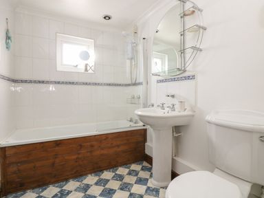 A bathroom with a bathtub with wooden paneling a pedestal sink a toilet and a round mirror on the wall at Trevean in Portreath
