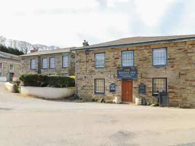 Stone building with The Bridge Inn sign and wooden door next to a street with bushes and other buildings in the background