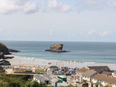 A beach with people swimming and sunbathing by the sea near a rock formation at Trevean in Portreath