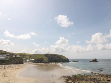 A beach with people on the sand and in the water with cliffs and houses in the background at Trevean in Portreath