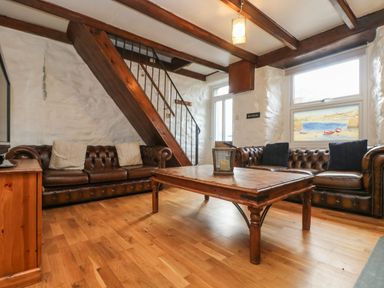 A living room with two brown leather sofas a wooden coffee table and wooden staircase at Trevean in Portreath