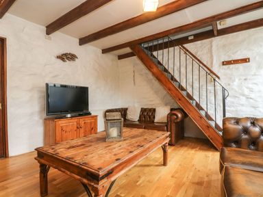 A living room with a wooden coffee table a television on a wooden cabinet and brown leather sofas under a staircase at Trevean in Portreath
