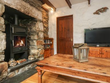 A living room with a stone fireplace and wood burning stove a wooden table with a lantern wooden door and a television on a wooden cabinet at Trevean in Portreath