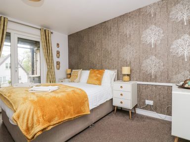 A bedroom with a double bed orange throw pillows bedside tables lamps and curtains at Devine Lodge in Callington