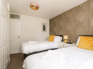 A bedroom with two single beds and a nightstand with a lamp and decorative items at Devine Lodge in Callington