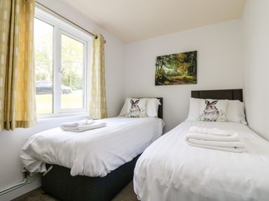 A bedroom with two single beds with rabbit pillows and folded towels under a window with yellow curtains at Devine Lodge in Callington