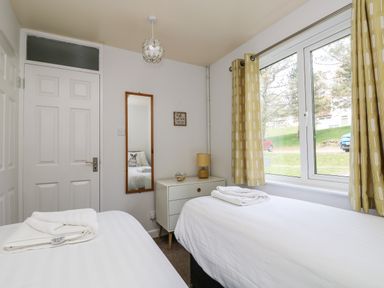A bedroom with two single beds a dresser with a lamp a wall mirror and a window with yellow curtains at Devine Lodge in Callington