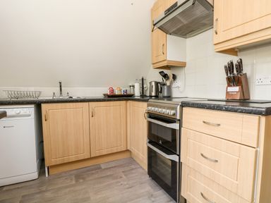 A kitchen with wooden cabinets a black countertop a stove a dishwasher and kitchen utensils at Devine Lodge in Callington