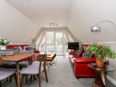 A living room with red sofas a dining table with chairs and glass doors leading to a balcony at Devine Lodge in Callington