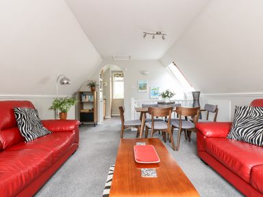 A living room with red sofas a wooden coffee table a dining table with chairs and a bookshelf at Devine Lodge in Callington
