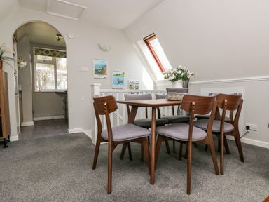 A dining area with wooden table and chairs next to a staircase and window at Devine Lodge in Callington