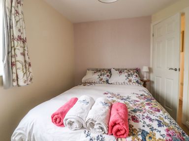 A bedroom with a bed with floral bedding towels on the bed and a lamp on a bedside table at The Old Hen Shed in Hainworth near Haworth